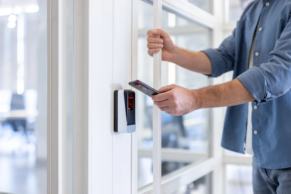 Une personne utilise un système de contrôle d'accès électronique mural, tenant une carte d'identification près du lecteur